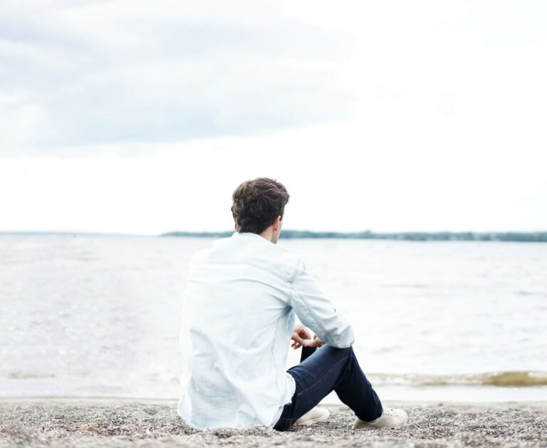 Man sitting on the beach looking out at the ocean